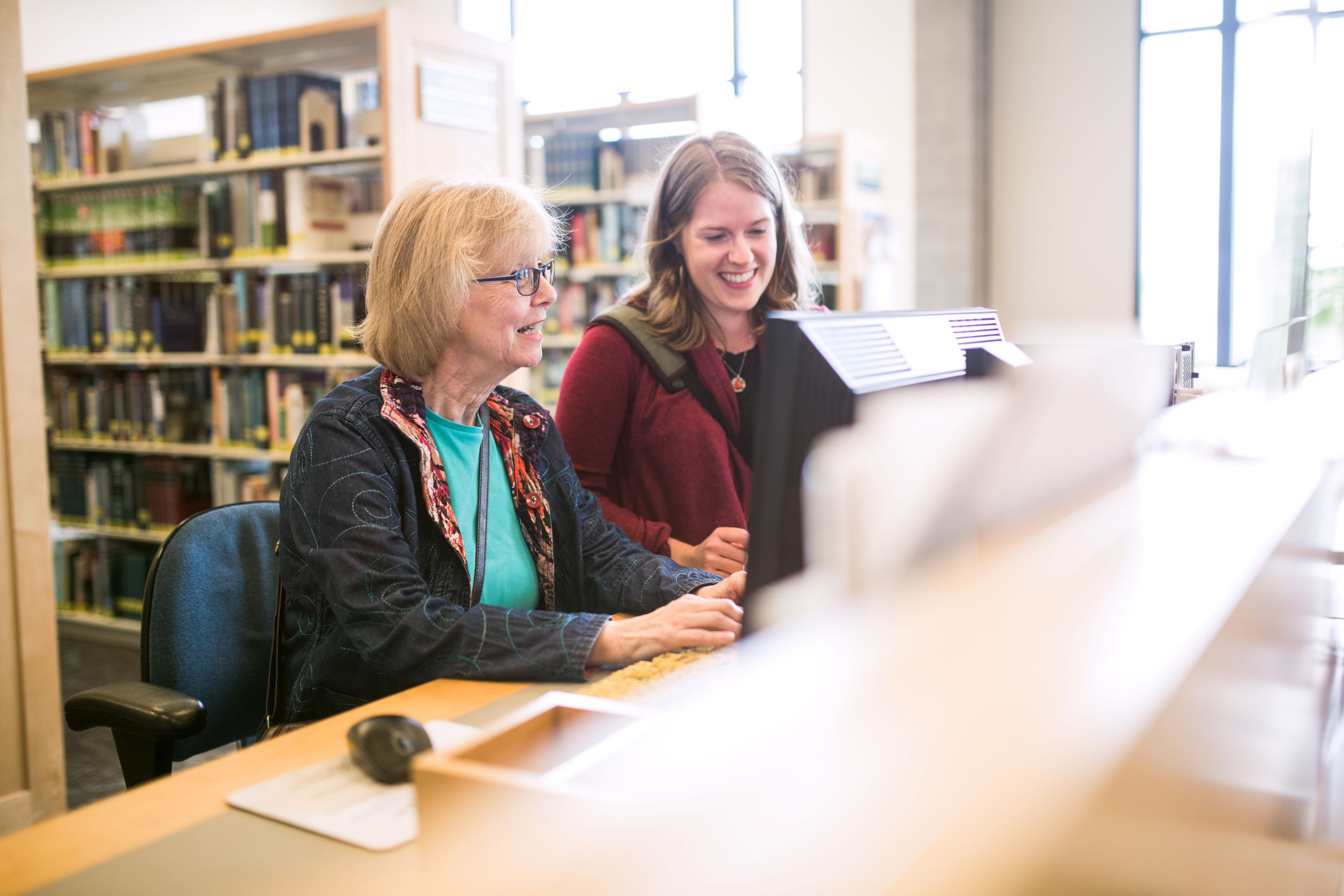 Two people sitting, smiling and working on the computer at a library.